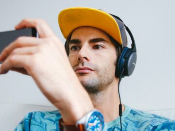man wearing black corded headphones while holding phone