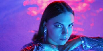 Beautiful woman posing in pool water under neon color light. Party, attractive chic in shining dress