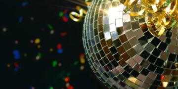 Shiny retro disco ball sparkling in the light with glittery ribbon and colorful confetti