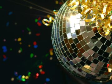 Shiny retro disco ball sparkling in the light with glittery ribbon and colorful confetti