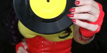 Woman in 1980s yellow clothing holding 45rpm record. Record label painted with yellow poster paint