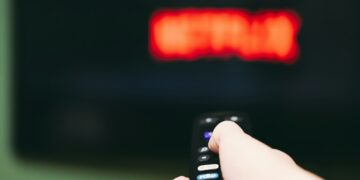 Woman using remote control to switch streaming service on television