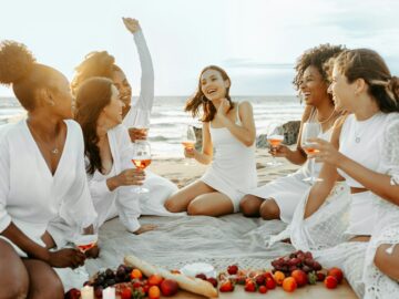 Excited female friends celebrating hen party, drinking wine, eating fresh fruits and chatting