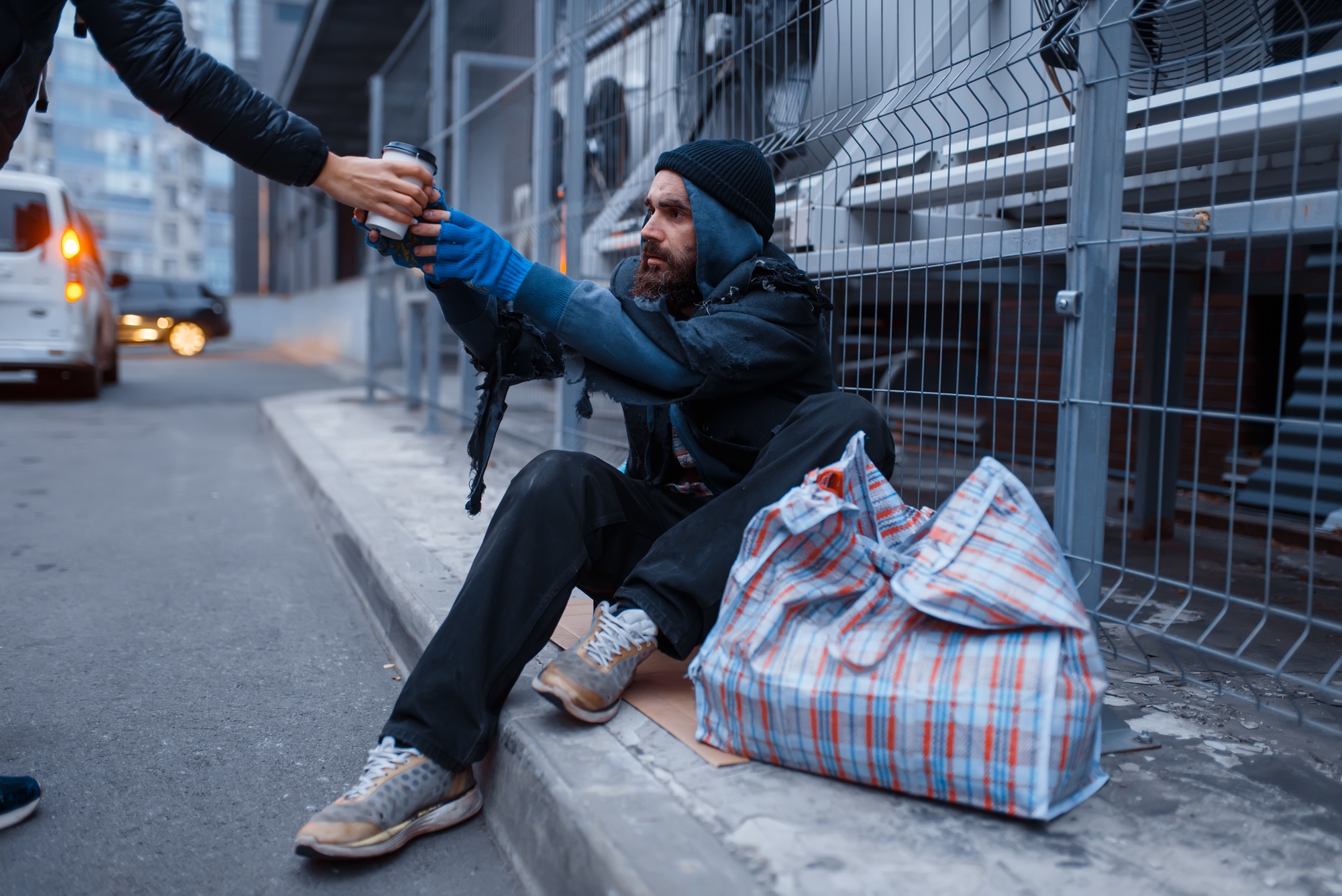 Male person gives cup of hot coffee to homeless